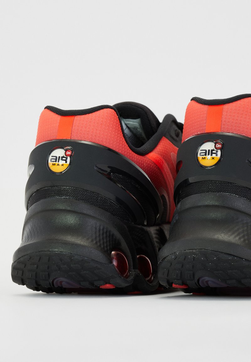 Zapatillas deportivas rojas y negras con una parte superior texturizada, suela de goma negra y detalle de amortiguación de aire que presenta un logo circular de aire.