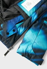 Veste rembourrée avec un extérieur noir et une doublure intérieure dégradée bleue. Comprend une fermeture éclair et deux boutons noirs.