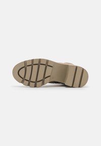 Tan rubber sole with a textured surface, featuring deep grooves and a rounded toe. Sturdy design suitable for various surfaces.