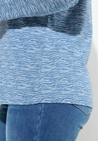 Top azul con un patrón de olas blancas, hecho de una tela suave. Combinado con jeans de mezclilla azules que muestran un diseño ajustado.