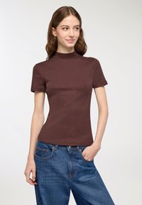 Top corto a maniche corte ribbed marrone con collo alto, abbinato a jeans in denim blu a vestibilità ampia. Texture liscia e silhouette aderente.