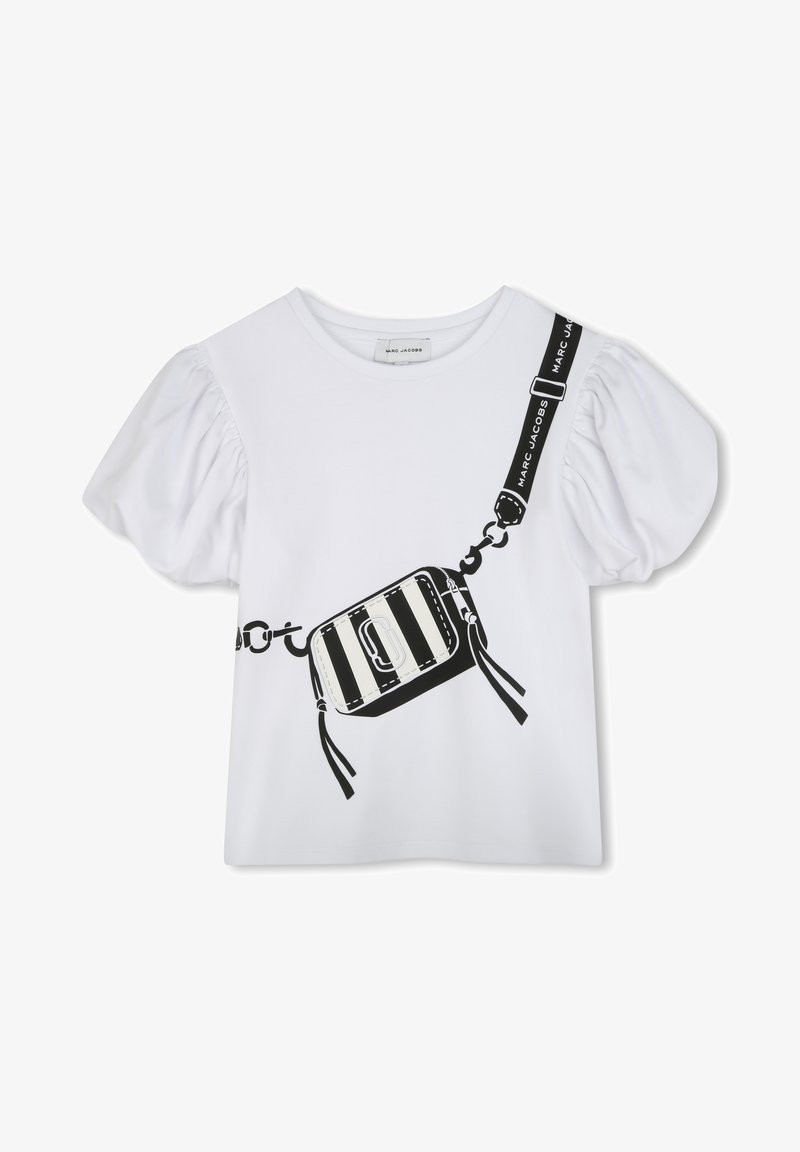 Camiseta blanca con mangas abullonadas y un gráfico negro de una bolsa a rayas con cadenas, acentuada por una correa con texto.