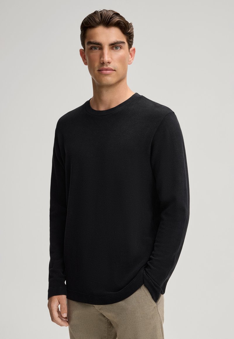 Schwarzes langärmliges Rundhals-Sweatshirt mit strukturierter Oberfläche, lockerer Passform und gerippten Bündchen, kombiniert mit beigen strukturierten Hosen.