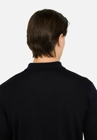 Polo in maglia blu navy con colletto e design della schiena senza cuciture, caratterizzato da una texture fine e un branding minimalista.