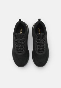 Baskets de sport noires avec une empeigne en maille, lacets plats avec des éclats blancs, marquage en relief et une semelle striée pour l'adhérence.