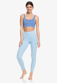 Lichtblauwe legging met hoge taille en een strakke pasvorm, gecombineerd met een blauwe gebloemde crop top. Beide gemaakt van rekbaar materiaal.