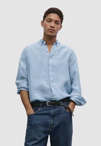 Light blue linen shirt with a button-down collar, rolled sleeves, and front buttons, paired with dark denim jeans and a braided belt.