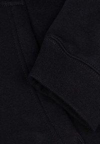 Le tissu d'un sweat à capuche noir montre un gros plan de la manche, mettant en avant une texture côtelée et des coutures soignées, soulignant son élasticité et sa durabilité.