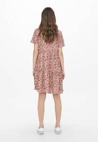 Kortärmad, rosa blommig klänning med lagerdesign, som har små mörka blommönster. Bärs med vita sneakers.