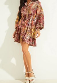 Robe boutonnée à manches longues avec motifs paisley multicolores, taille cintrée et ourlet à volants, associée à des chaussures à plateforme blanches.