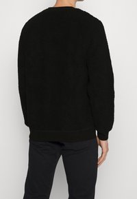 Felpa nera in pile con superficie texturizzata, maniche lunghe e scollatura a girocollo. Presenta polsini e orlo a coste. Design semplice, senza motivi.