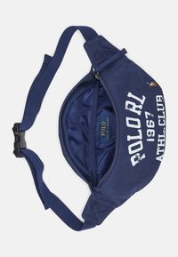 Marinblå kanvasbältesväska med dragkedjestängning, justerbar rem och vit tryckt text. Inuti finns en enfärgad blå foder.