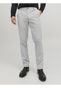Pantaloni grigi chiaro su misura realizzati in tessuto morbido, dotati di chiusura con bottone, tasche laterali e un design slim fit. Abbinati a stivaletti neri alla caviglia.