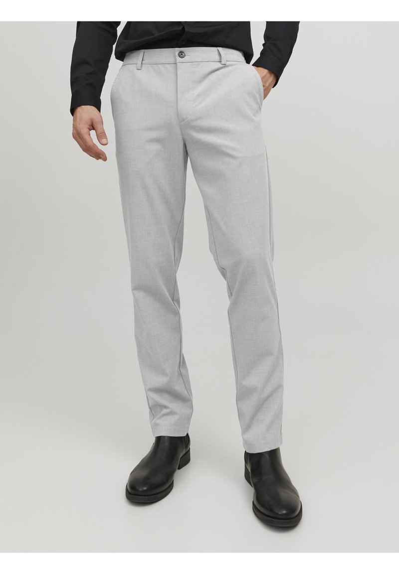 Pantaloni grigi chiaro su misura realizzati in tessuto morbido, dotati di chiusura con bottone, tasche laterali e un design slim fit. Abbinati a stivaletti neri alla caviglia.