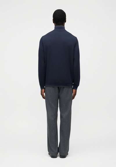Μπλε ναυτικό φούτερ με ψηλό γιακά, υφασμάτινη υφή και ριμπ μανσέτες, συνδυασμένο με γκρι, φαρδιές υφασμάτινες παντελόνες.
