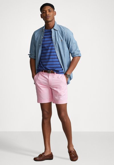 Denim srajca s gumbi, mornarsko modra in modra črtasta majica, roza kratke hlače, rjavi loafers, in ura. Sproščena obleka z različnimi teksturami in barvami.