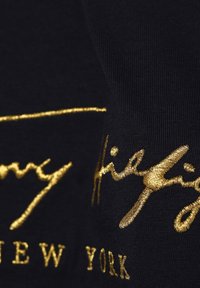 Tela negra con texto bordado en oro que presenta un estilo de firma y el detalle "NUEVA YORK", destacando una textura suave y líneas limpias.