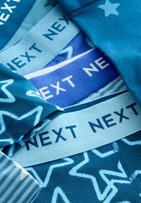 Vêtements pliés tons bleus avec ceintures élastiques affichant le nom de la marque "NEXT" dans différentes nuances et motifs d'étoiles.