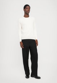 White, long-sleeve sweater with a round neck, paired with black, wide-leg trousers. Footwear is black leather shoes. Plain background.