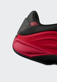 Teniska s černo-červeným designem, hladkým syntetickým materiálem, zaobleným tvarem, texturovanými detaily a polstrovaným patním dílem pro podporu.