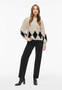 Krémový pletený svetr s diamond vzory v černé a zelené barvě, spárovaný s černými rovnými džínami a kotníkovými botami na podpatku.