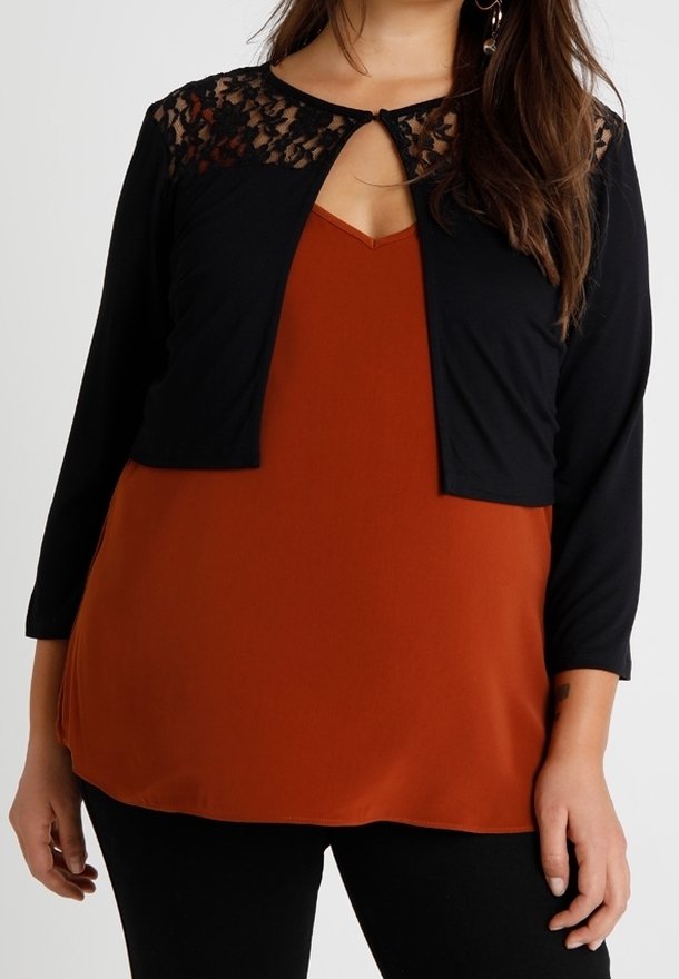 Femme portant un top orange rouille avec un cardigan court noir avec des détails en dentelle sur les épaules et des manches trois-quarts.