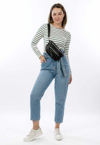 Borsa a tracolla nera in pelle con tasche con zip, indossata sopra una camicia a maniche lunghe a righe e jeans blu a vita alta. Sneakers bianche ai piedi.