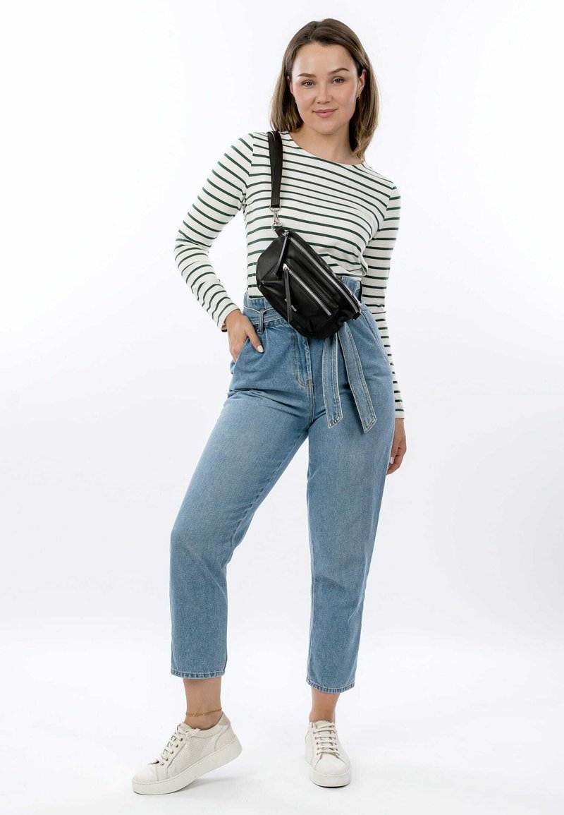 Borsa a tracolla nera in pelle con tasche con zip, indossata sopra una camicia a maniche lunghe a righe e jeans blu a vita alta. Sneakers bianche ai piedi.