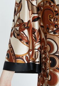 Braunes Seidengewebe mit abstrakten Mustern, das einen schwarzen Satinabschluss hat. Die Textur ist glatt und reflektiert das Licht sanft.