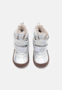 Botas de tobillo holográficas plateadas con dos correas ajustables de Velcro, forro beige suave y suelas de goma marrón. Diseño de punta redondeada.