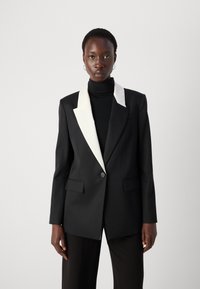 Black blazer with a white peak lapel, single button closure, and front pockets; features a tailored fit and smooth fabric texture.