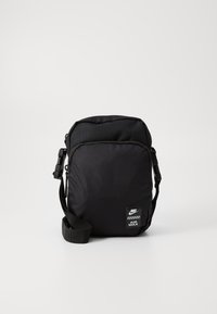 Bolso negro Nike Air Max, hecho de nylon texturizado, con correa ajustable y parche del logo. Forma rectangular compacta con cierre de cremallera.