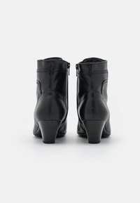 Botines de cuero negro hasta el tobillo con cremallera lateral, forma contorneada y un tacón bloque moderado. Textura suave con detalles de costura visibles.