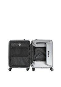 Valigia grigia con guscio rigido, quattro ruote, interno nero e più scomparti. Un lato presenta tasche in rete e una cerniera.