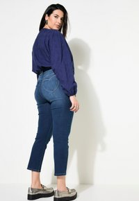 Marinblå blus med puffärmar, kombinerad med högmidjade blåjeans som har en hjärtformad bakficka. Metalliska skor.