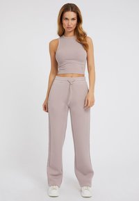 Přiléhavý žebrovaný crop top v jemné taupe, spárovaný s volnými taupe tepláky se širokým elastickým pasem a bílými teniskami.