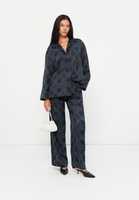 Navy patterned ensemble featuring a loose button-up shirt and wide-leg pants. A small white pleated handbag and pointed black heels complete the look.