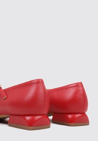 Bailarinas de cuero rojo con un tacón bajo y un acabado suave. Presentan un diseño simple con punta redondeada y acentos de hardware mínimos.