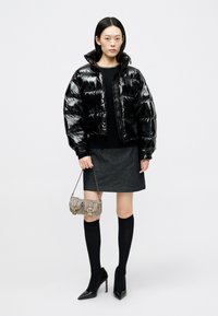 Φουσκωτό μαύρο τζάκετ μπομπέρ, εφαρμοστό πλεκτό μπλουζάκι, γκρι τζιν φούστα, μαύρες κάλτσες μέχρι το γόνατο, μυτερές μαύρες γόβες, μικρή μεταλλική τσάντα ώμου.