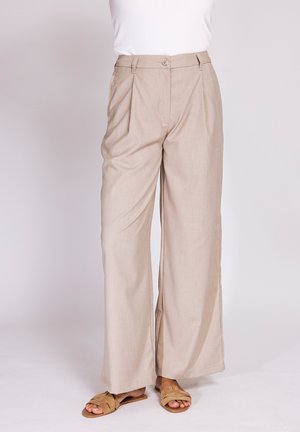 Beige high-waist wide-leg pants with front button and zipper, worn with a white top and tan open-toe flat sandals.