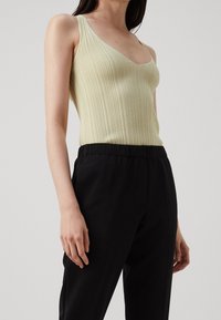 Débardeur léger vert clair à côtes avec un décolleté en V profond et des bretelles fines, associé à un pantalon avec taille élastique noir. Tissu texturé visible.