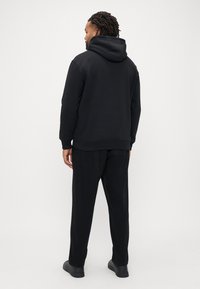 Hanorac negru cu glugă, cu croială lejeră, asortat cu pantaloni negri largi. Material neted, cu manșete și talie din material nervurat. Design minimalist.