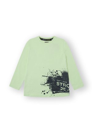 Camiseta de manga larga en algodón verde claro con estampado de salpicaduras negras y texto "ESTD 1953 STRONG". Cuello redondo clásico y textura suave.