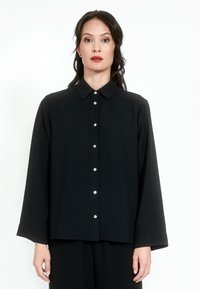 Black button-up shirt with a pointed collar, long sleeves, and front button closure featuring contrasting buttons. Smooth fabric texture.