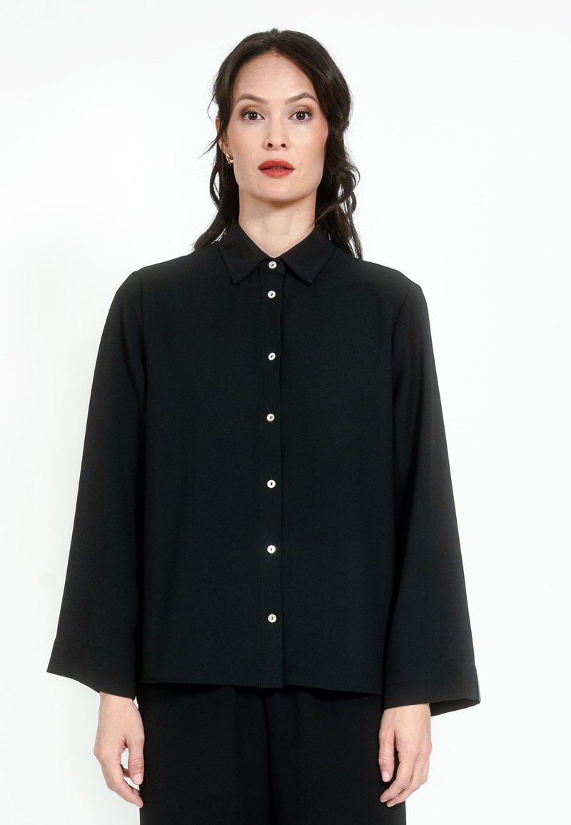 Black button-up shirt with a pointed collar, long sleeves, and front button closure featuring contrasting buttons. Smooth fabric texture.