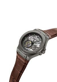 Skeleta pulkstenis ar pelēku nerūsējošā tērauda korpusu, brūnu krokodila raksta ādas siksniņu un redzamām iekšējām sastāvdaļām ar sudraba un zelta akcentiem.