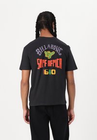 Zwarte katoenen t-shirt met kleurrijke grafische tekst op de achterkant, waaronder "Billabong," "Surf Africa," en "1640." Korte mouwen, casual pasvorm.