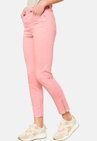 Jeans attillati rosa con dettaglio zip alla caviglia, caratterizzati da una texture liscia e un classico design a cinque tasche. Abbinati a sneakers beige.