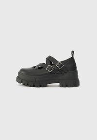 Black platform shoes with a chunky sole, featuring cross straps and buckles. Made of smooth material with a matte finish.