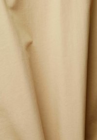 Tessuto beige con morbide pieghe e leggere rughe, che mostra una texture liscia e variazioni di sfumature delicate.
